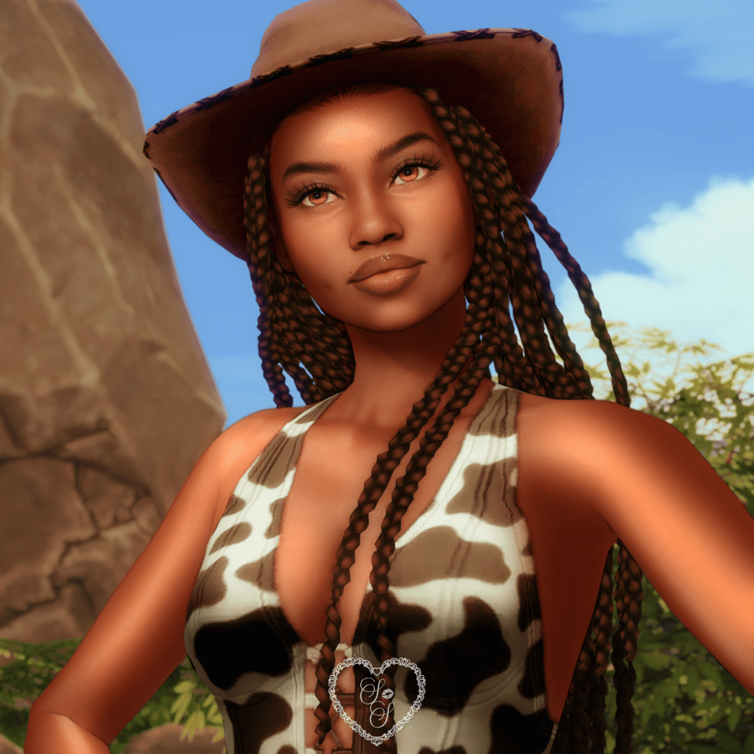 Close-up of Amara showcasing her cowprint Bonnie top, Callie hat, and long box braids against a clear blue sky and mountain backdrop.