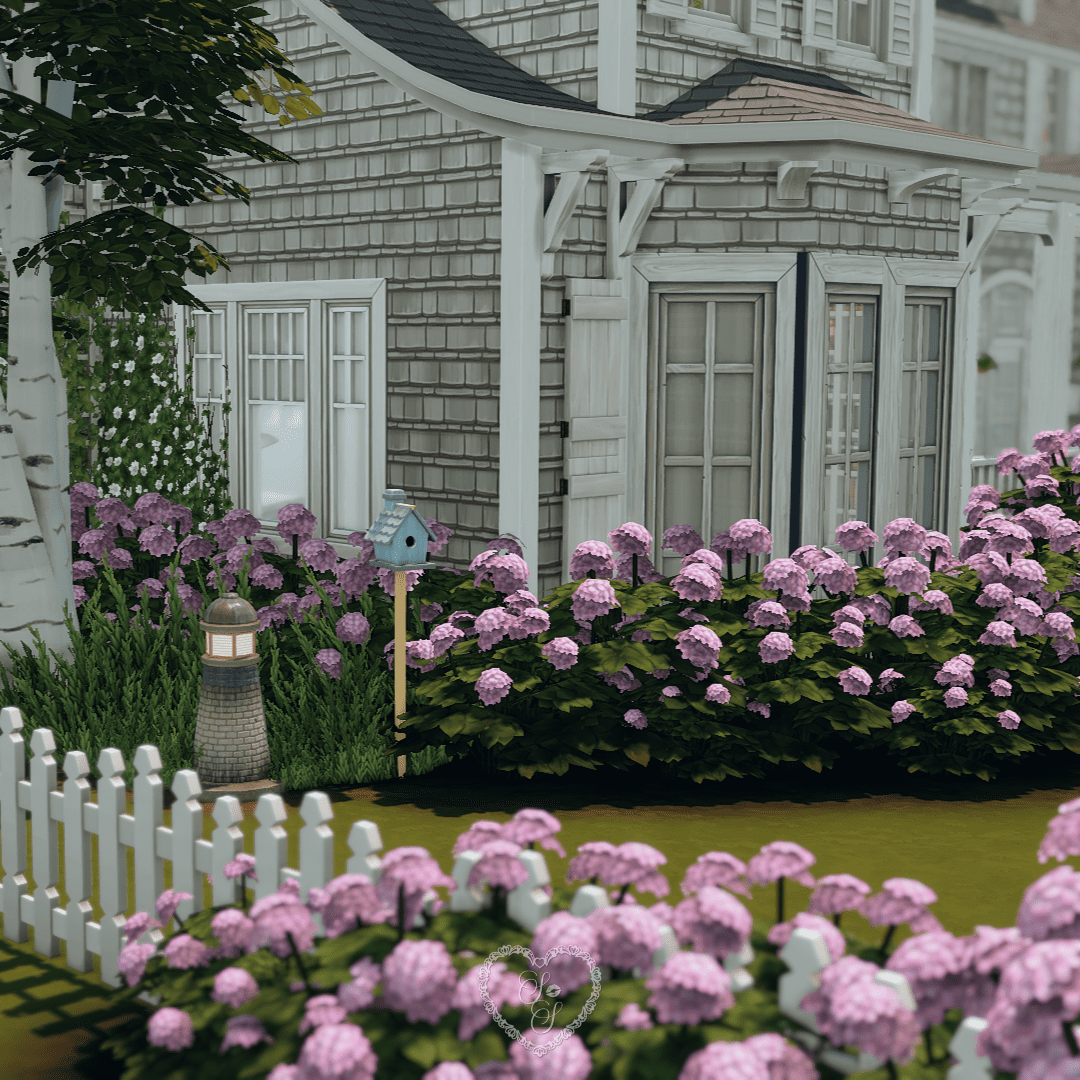 A cozy corner of the yard with white fencing, lavender hydrangeas, and a decorative birdhouse nestled in the landscaping.